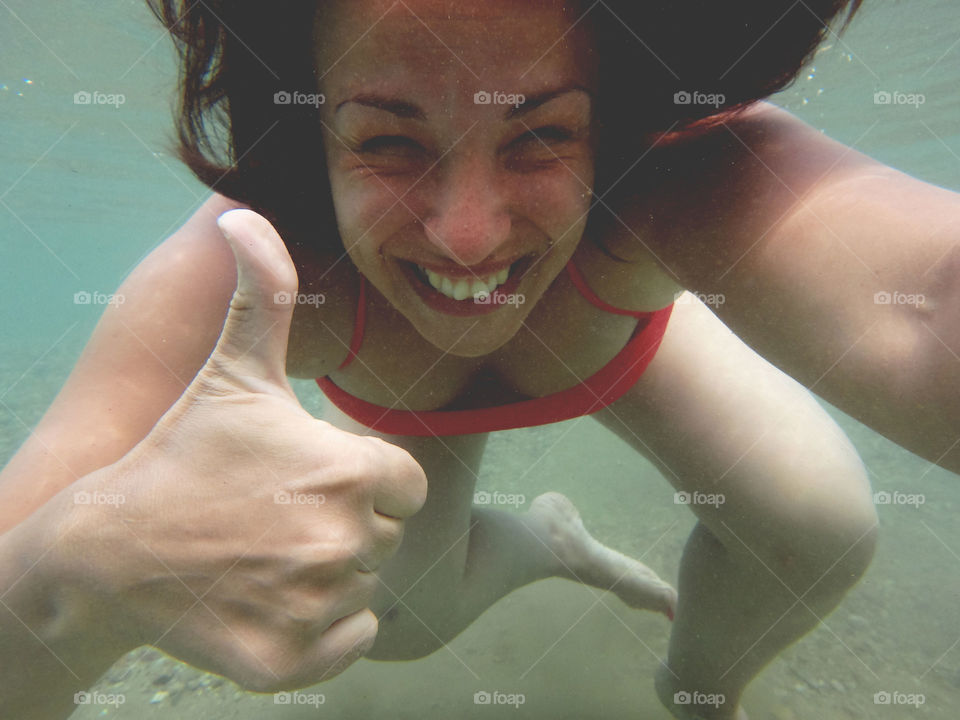 happy girl underwater. happy smiling girl underwater pointing ok hand sign