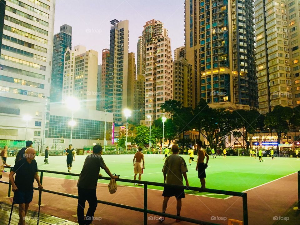 Night time soccer in a concrete field in the middle of Hong Kong’s bustling, crowded streets. Competition, camaraderie, and collectiveness.  