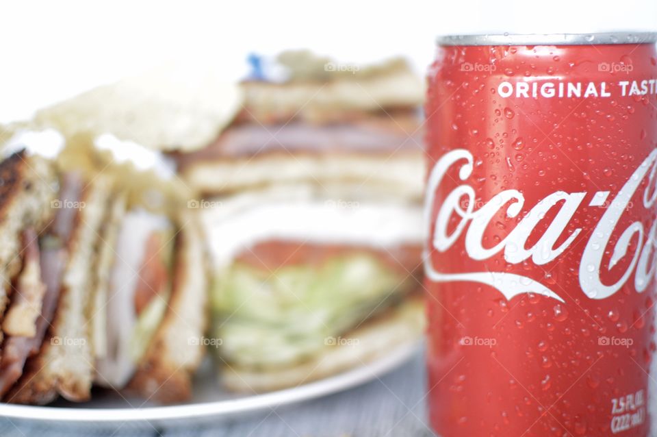 A can and a Bottle of Coca Cola with a club sandwich on a white rustic background 