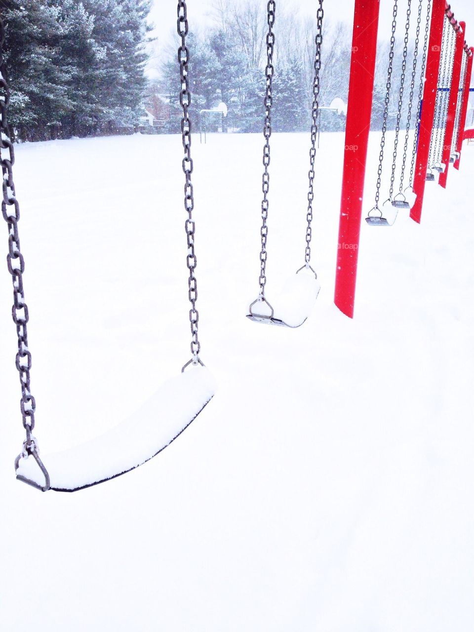 Swings covered in snow with contrasting red supports