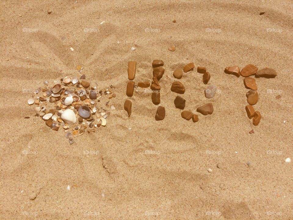 HOT letters with stones and shells on a sand