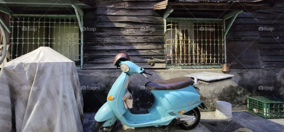 A water blue motorcycle parked outside a wooden house