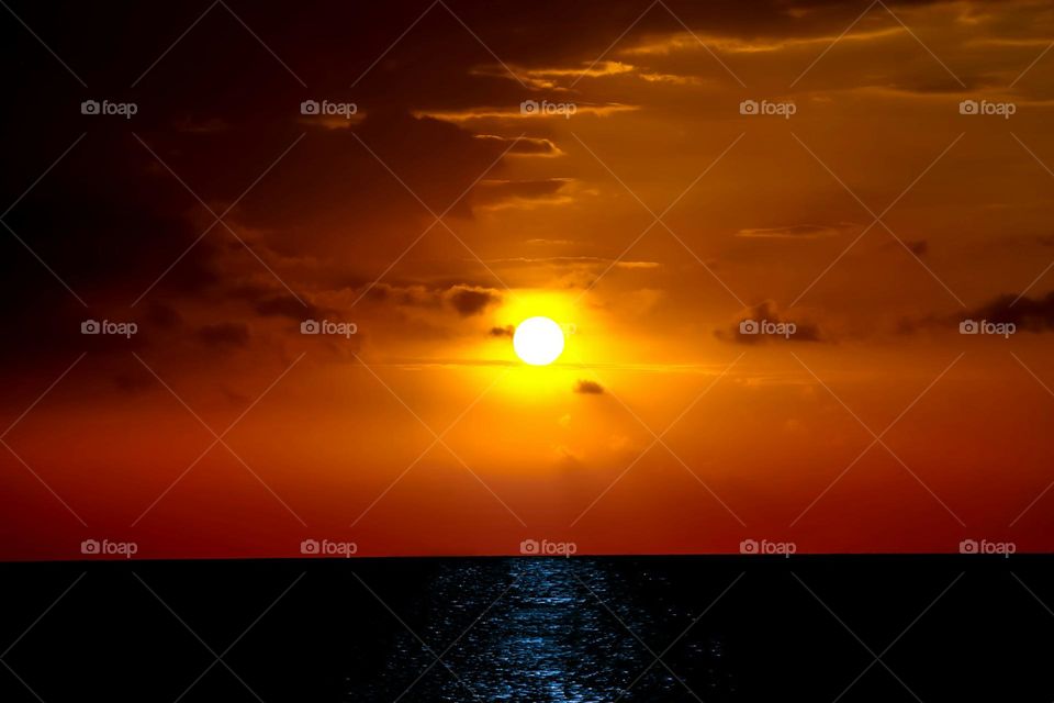 the sun is setting over the ocean on a cloudy day