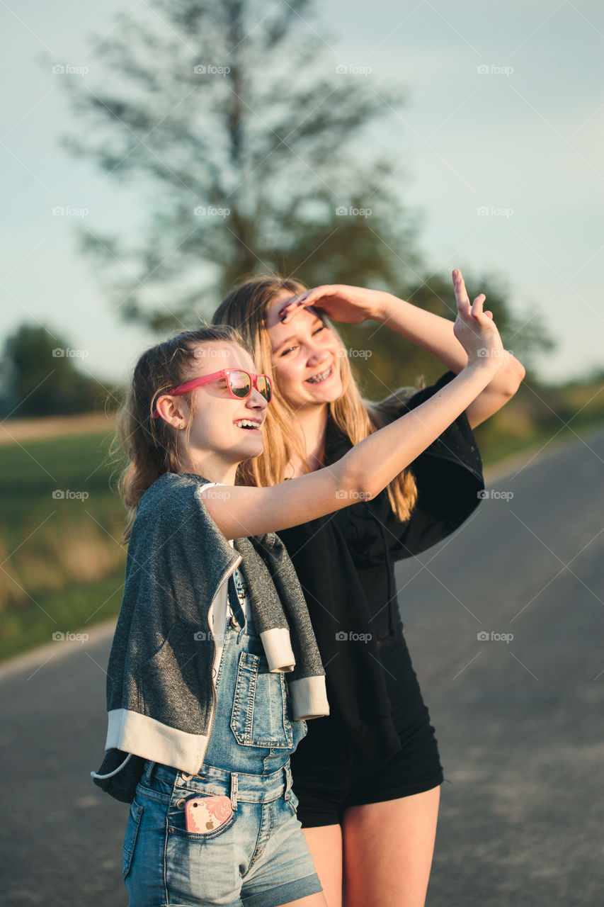 Teenage smiling happy girls having fun walking outdoors, hanging, spending time together on summer day. Real people, authentic situations