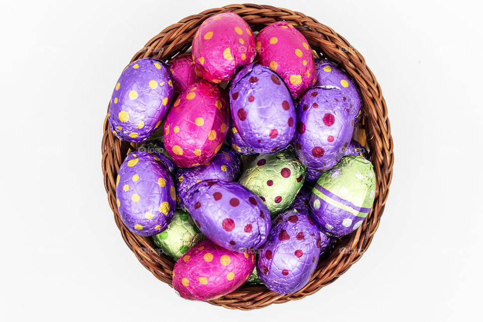 colorful chocolate Easter eggs in a brown woven wooden basket, placed against a white background