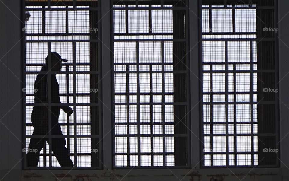 A silhouette of a man walking along an overhead passageway connecting two New York City Subway Station in Brooklyn, NYC.
