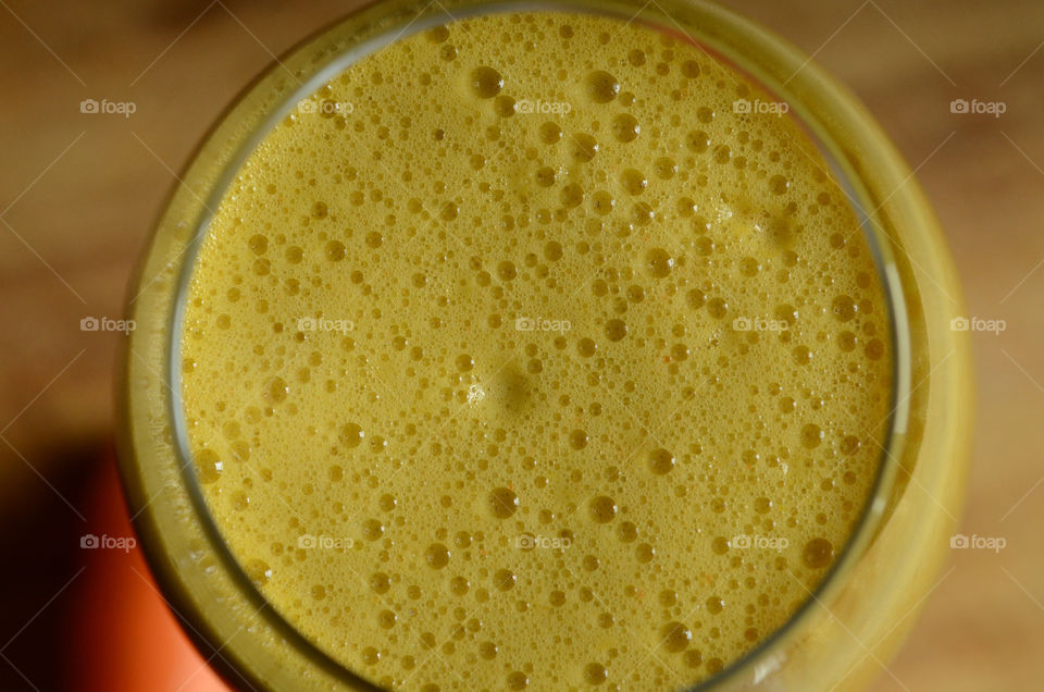 A fresh homemade glass of juice containing honeydew melon, ginger, and oranges is seen overhead bubbling forth its fresh froth.