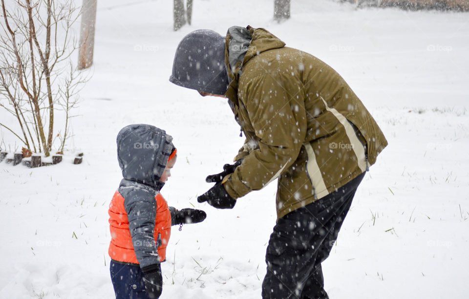 Father helping toddler boy in the snow outdoors