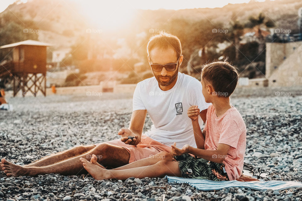 Father and son sitting on the beach at the sunset
