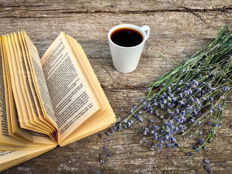 Open book with lavender and cup of coffee beside placed on wooden table