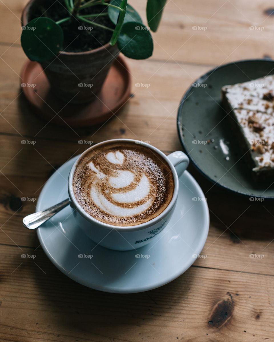 Coffee, cake and a plant on a table with latte art on the coffee