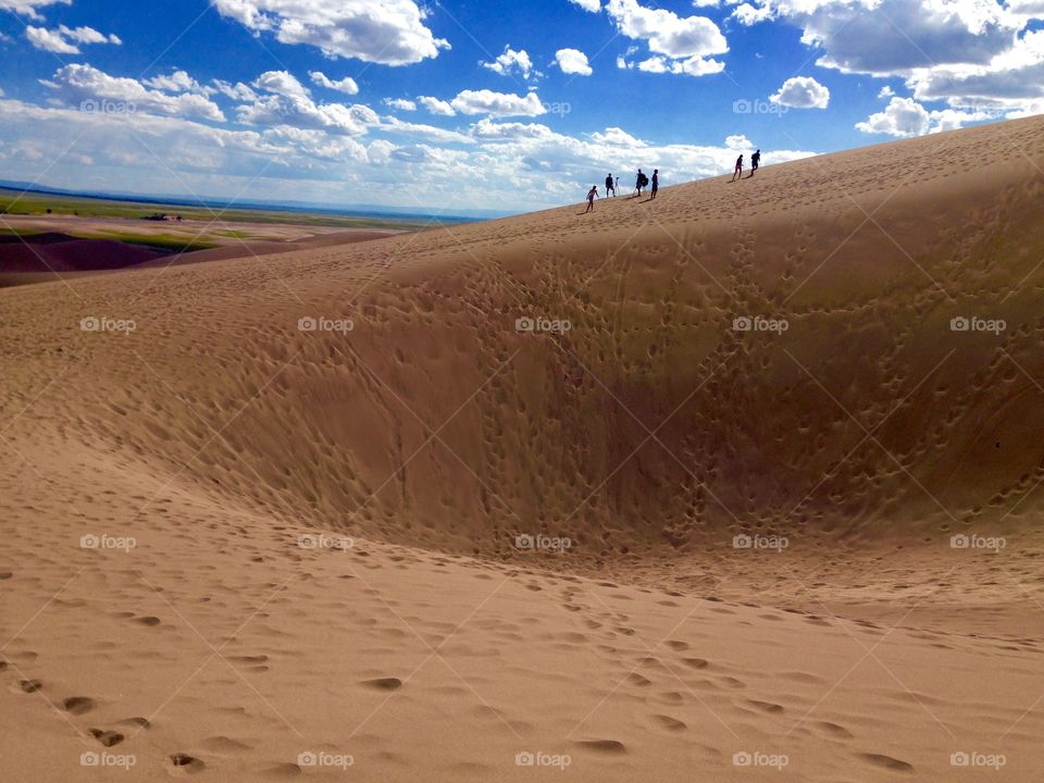 Climbing Giant Sand Dune. People enjoy huge sand dunes under a beautiful blue sky. 