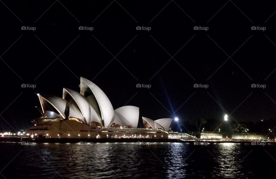 Light la from the Sydney Opera House are reflected onto the water at nighttime