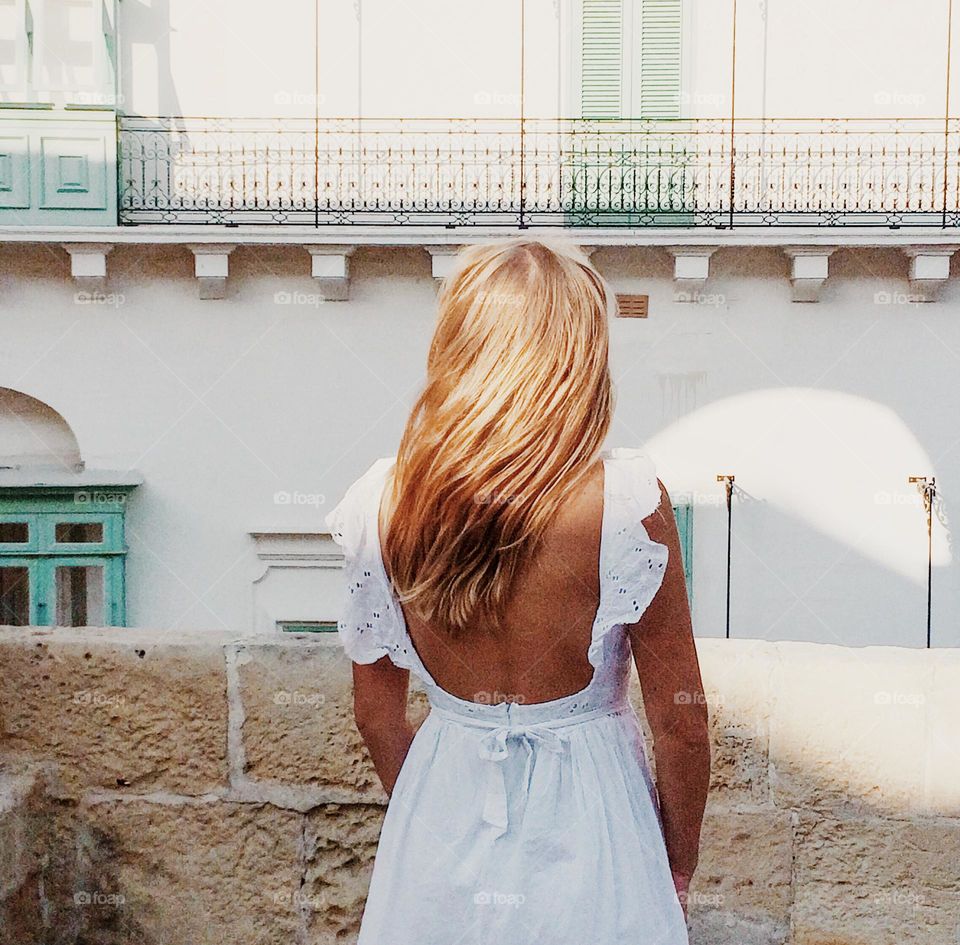 View from behind woman in a white dress standing next to the white building 