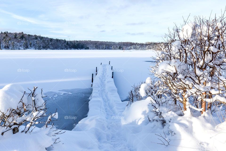 Wooden pier in frozen lake covered in deep white snow on a beautiful cold winter day 