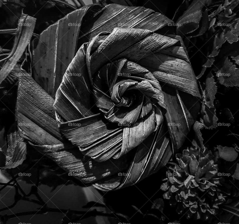 A flax flower that has been weaved out of dried flax leaf included in an arrangement. Black and white effect.