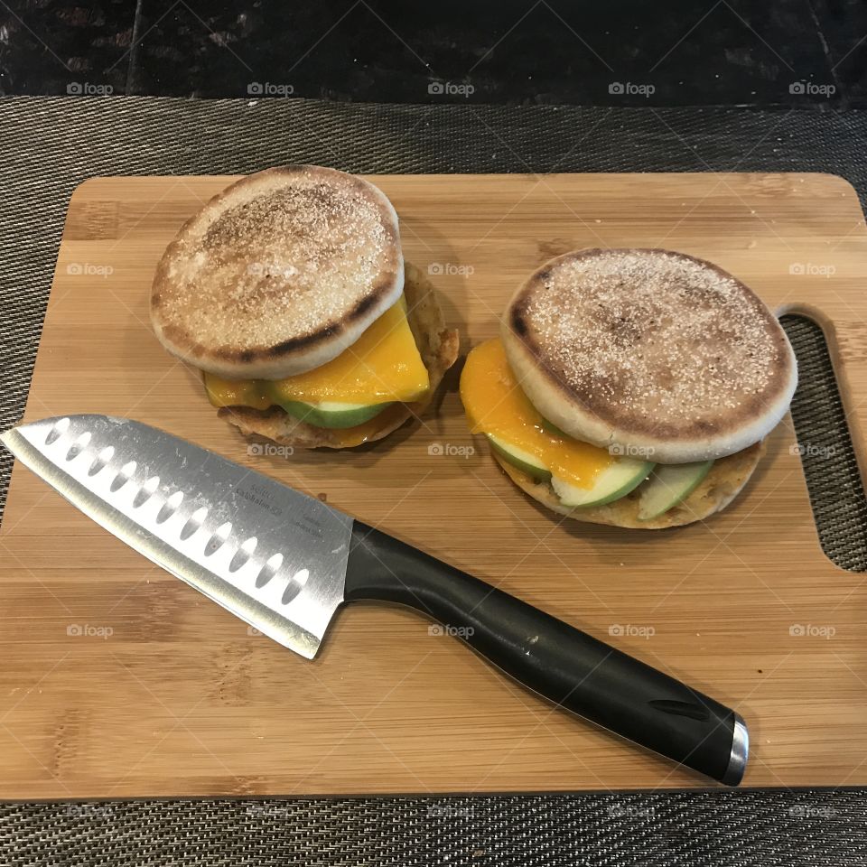 A yummy display of two apple and cheese melt sandwiches on English muffins displayed on a cutting board being prepared for a healthy meal in the kitchen. USA, America