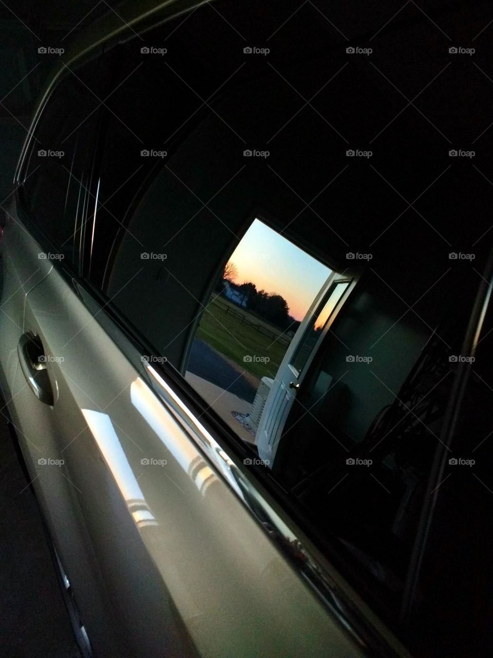 sunset through a doorway reflected in a car window in a garage