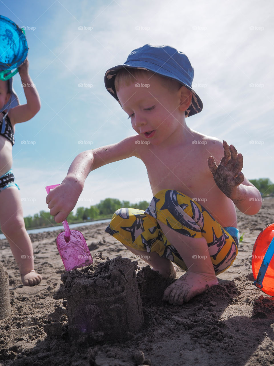 Toddler boy smashing his sandcastle with a pink shovel.