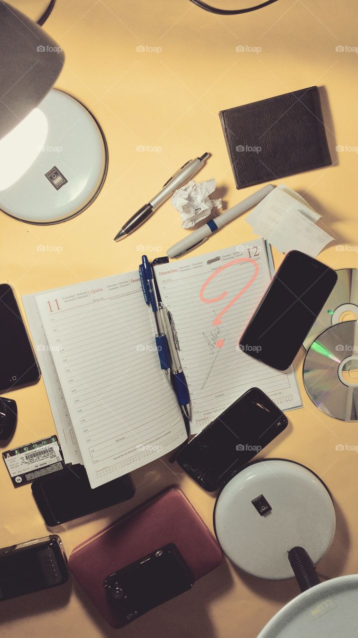 Escritório. Mesa, agenda, calendário, canetas, luminárias, calculadoras, celulares.
