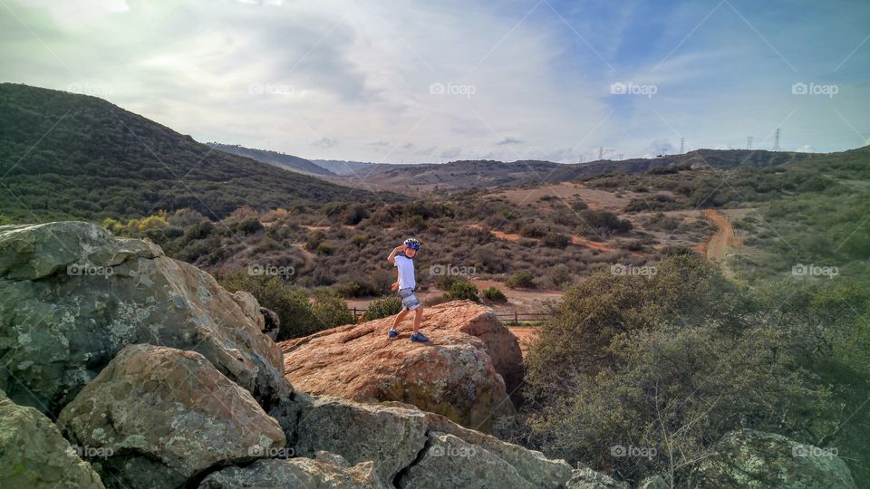 Boy with helmet saluting on top of rock
