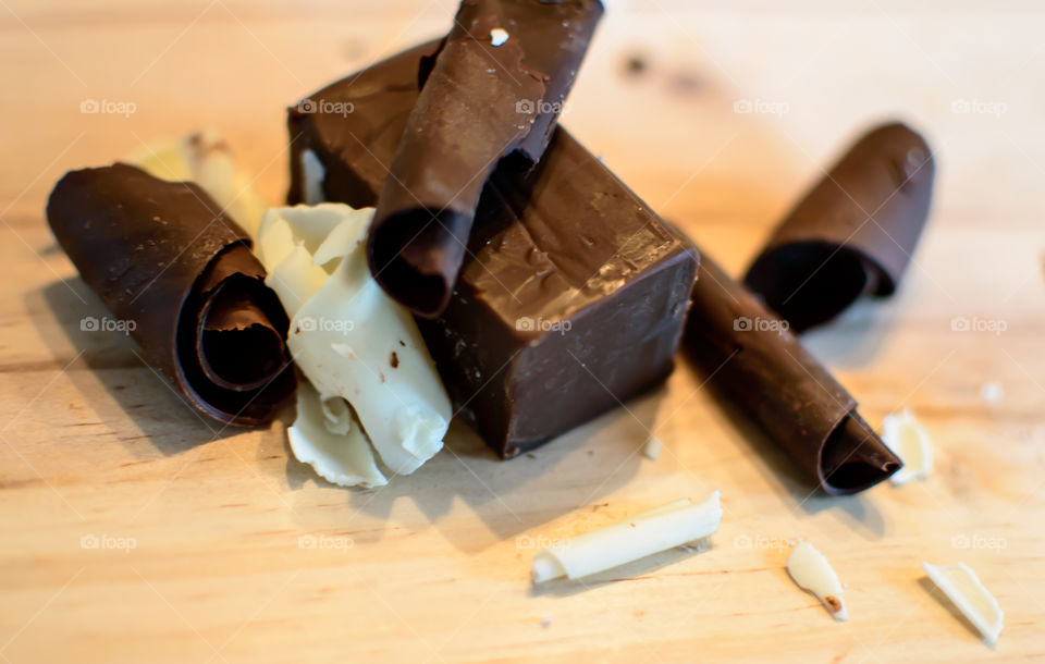 Dark chocolate block with white chocolate shavings and dark chocolate swirl pieces on wood background decadent gourmet photography 