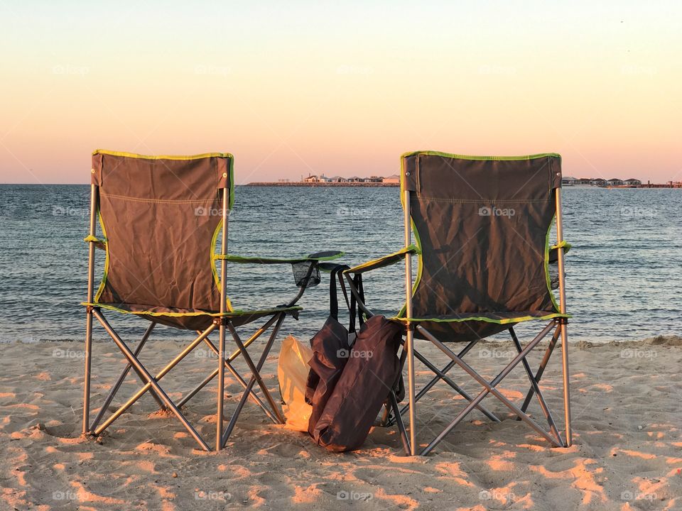 Two empty beach chairs facing the sea during the golden hour