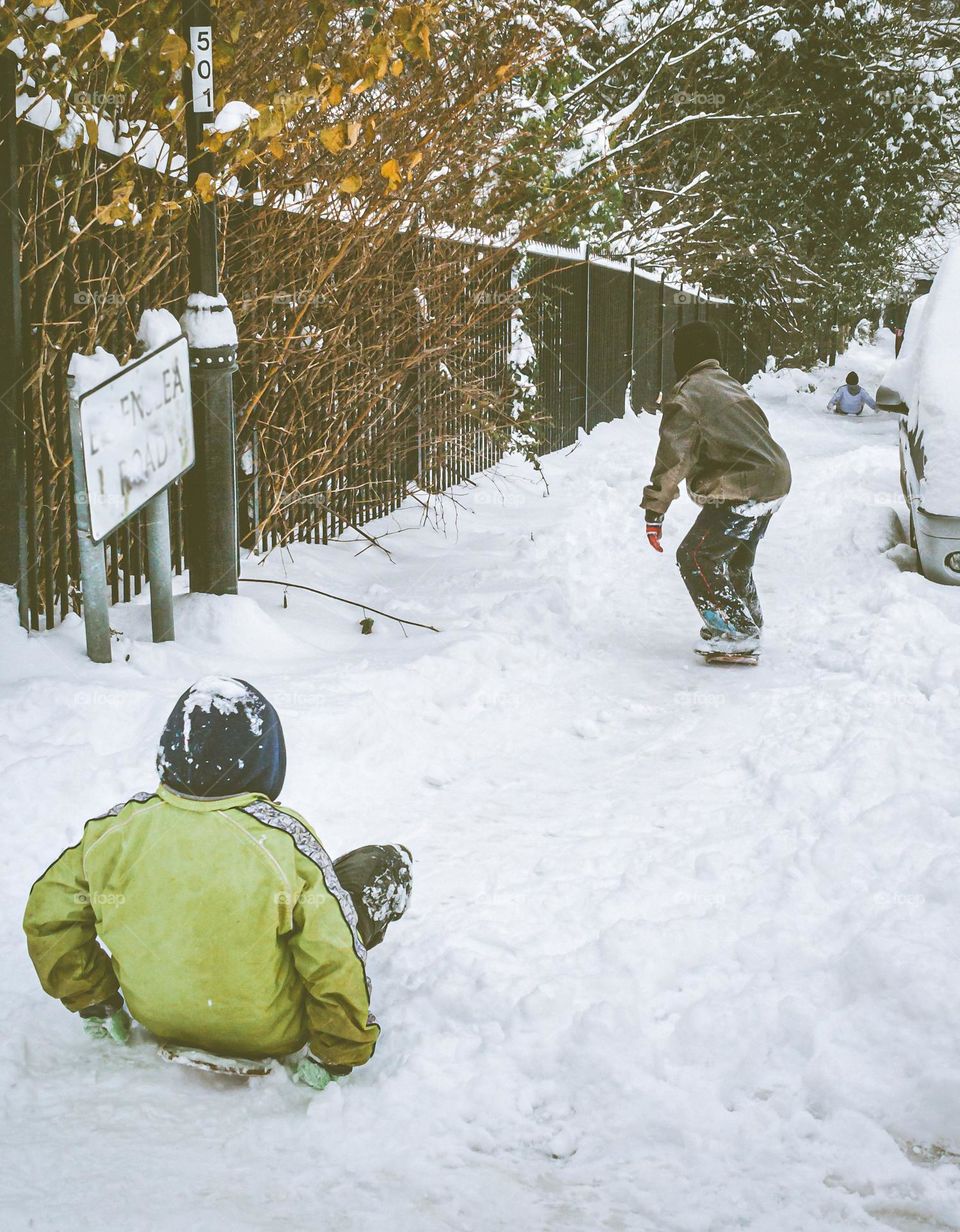 Kids snowboarding down a snow covered residential street