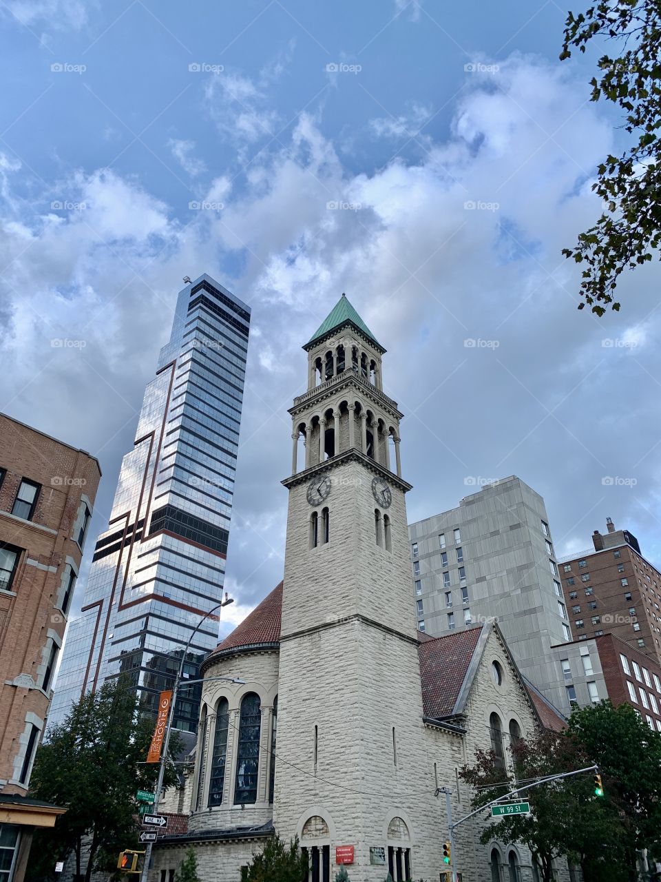 A church with two clocks side by side. Blue sky, clouds, other building in glass.