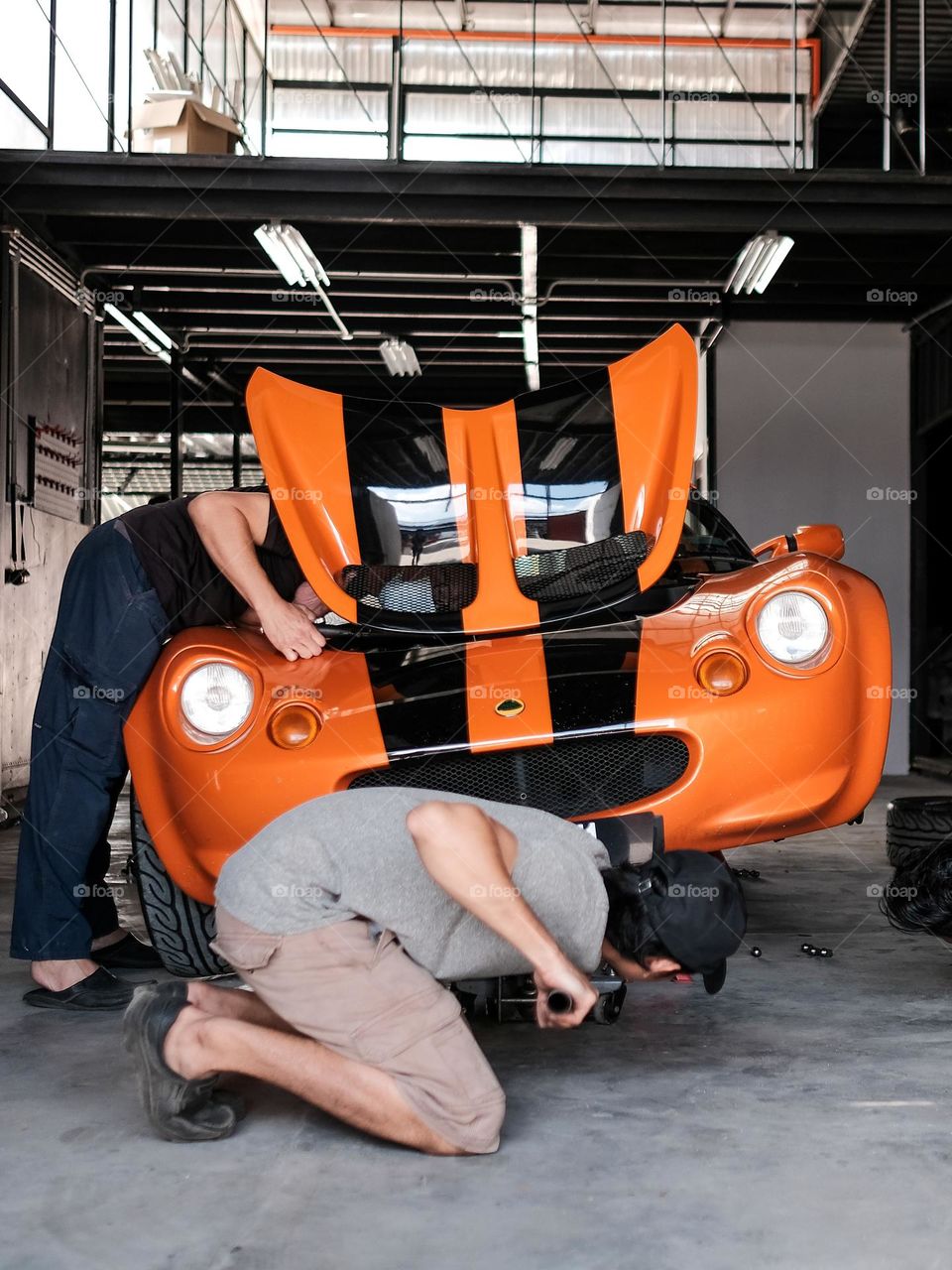 Two mechanic working on an orange sports car