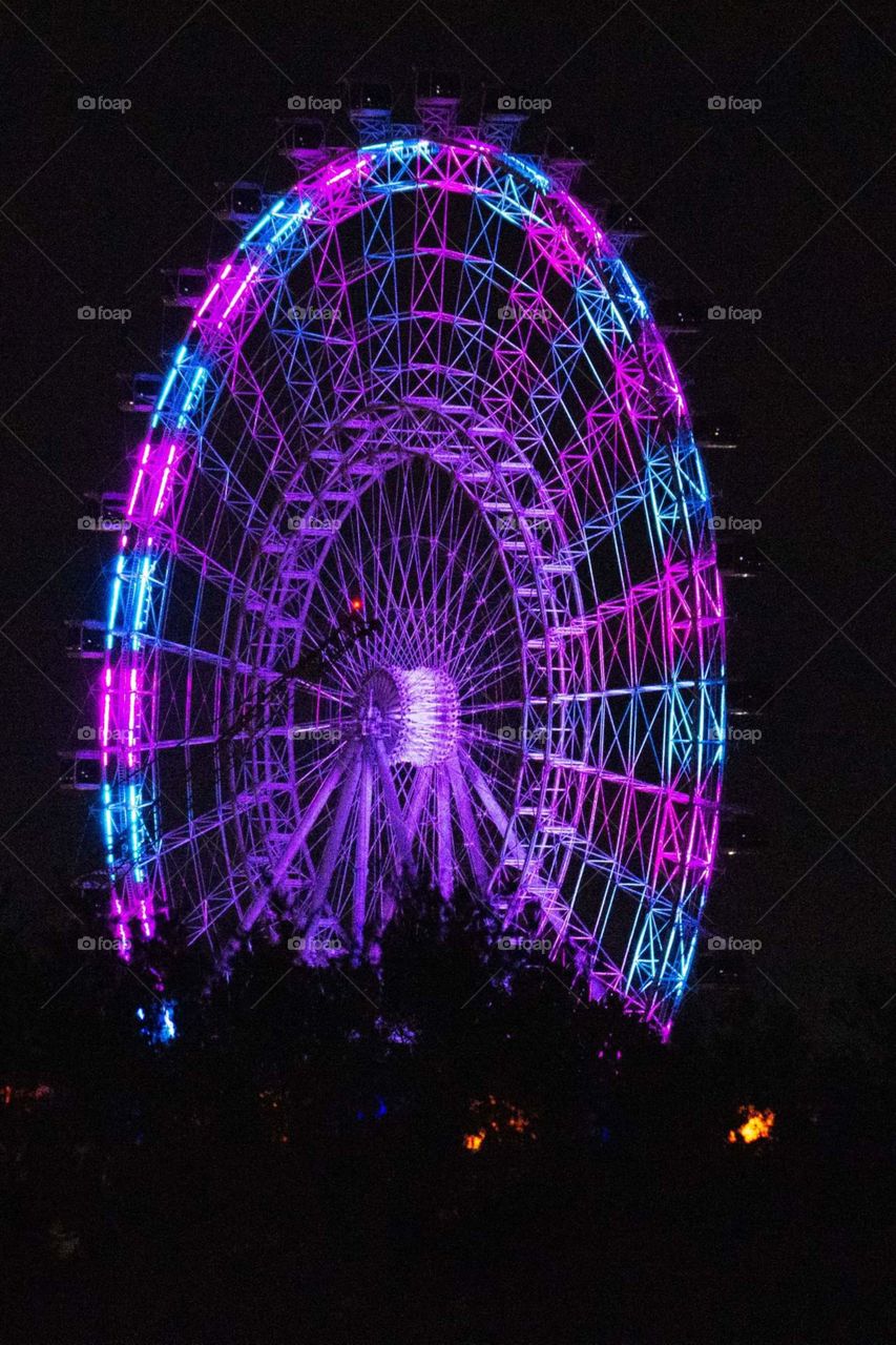 a ferris wheel with beautiful bright colors of pink and blue lights alternating against a black night sky