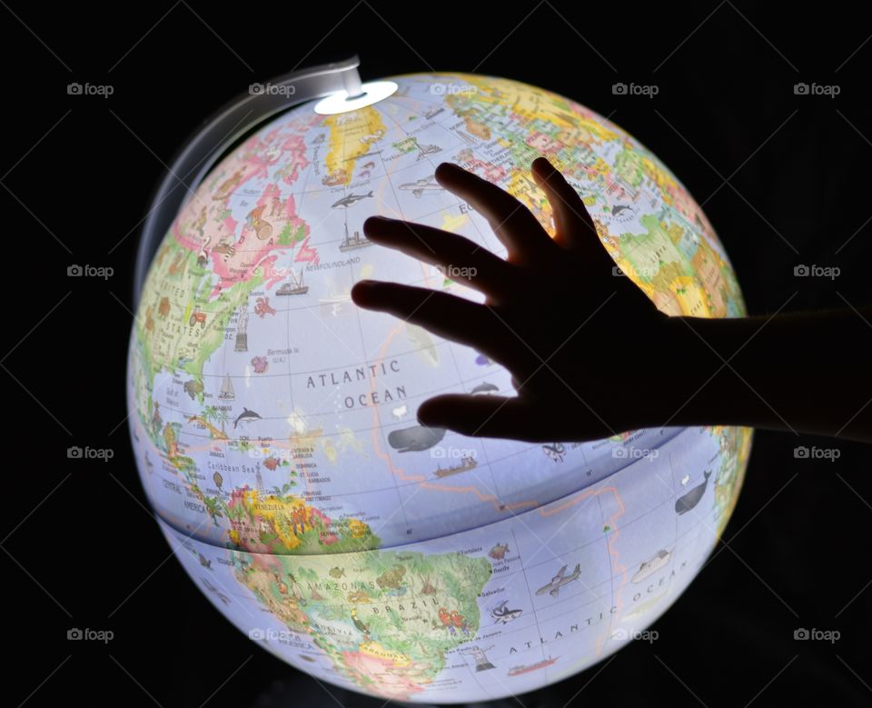 This is an image of a child's hand on an illuminated globe of the Earth with black backdrop.