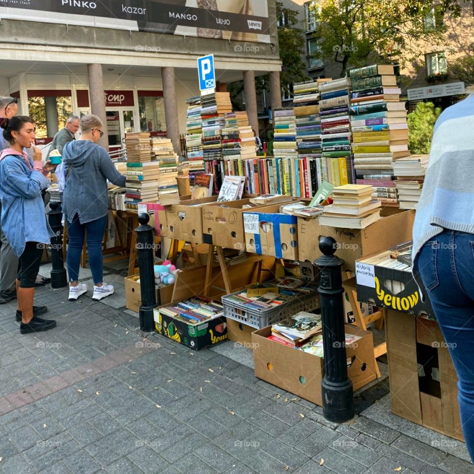 Sidewalk book sale outside a book store in Street. Books piled up on tables & in boxes with people buying books at low prices. Yard sale in summer with people buying books.