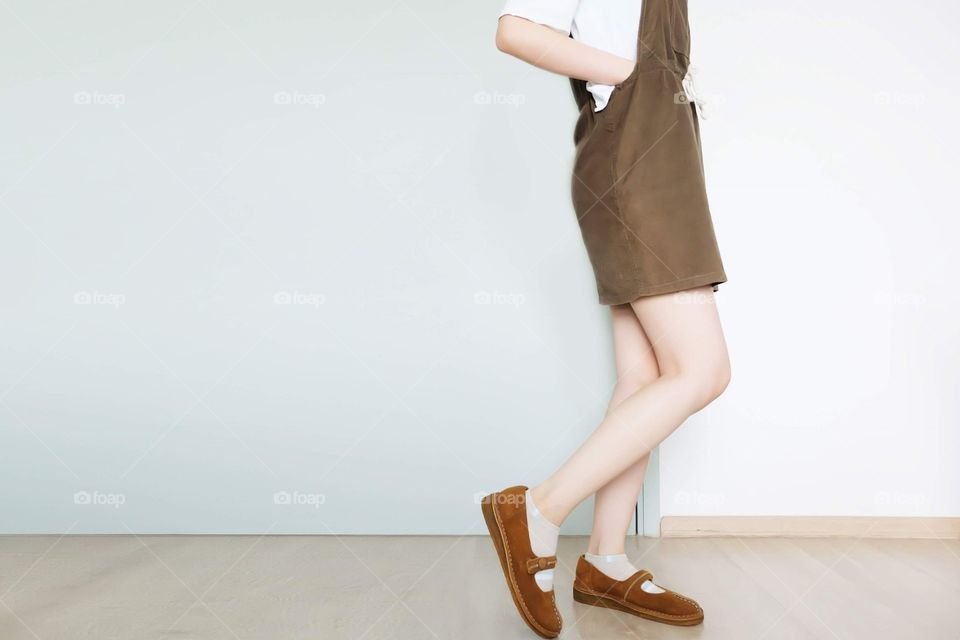 Portrait Female Slim Legs. Girl Sexy Long Leg. Beautiful Woman in Brown Dress and Brown Shoes Standing and Posing in The White Room at Home Background Great for Any Use.