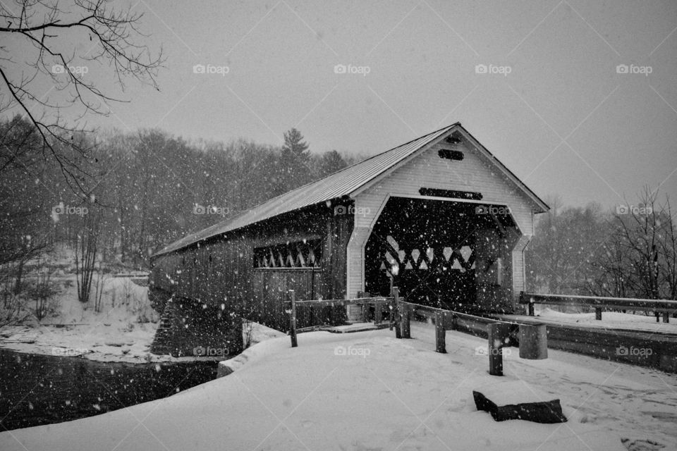 A covered bridge being gently blanketed with snow