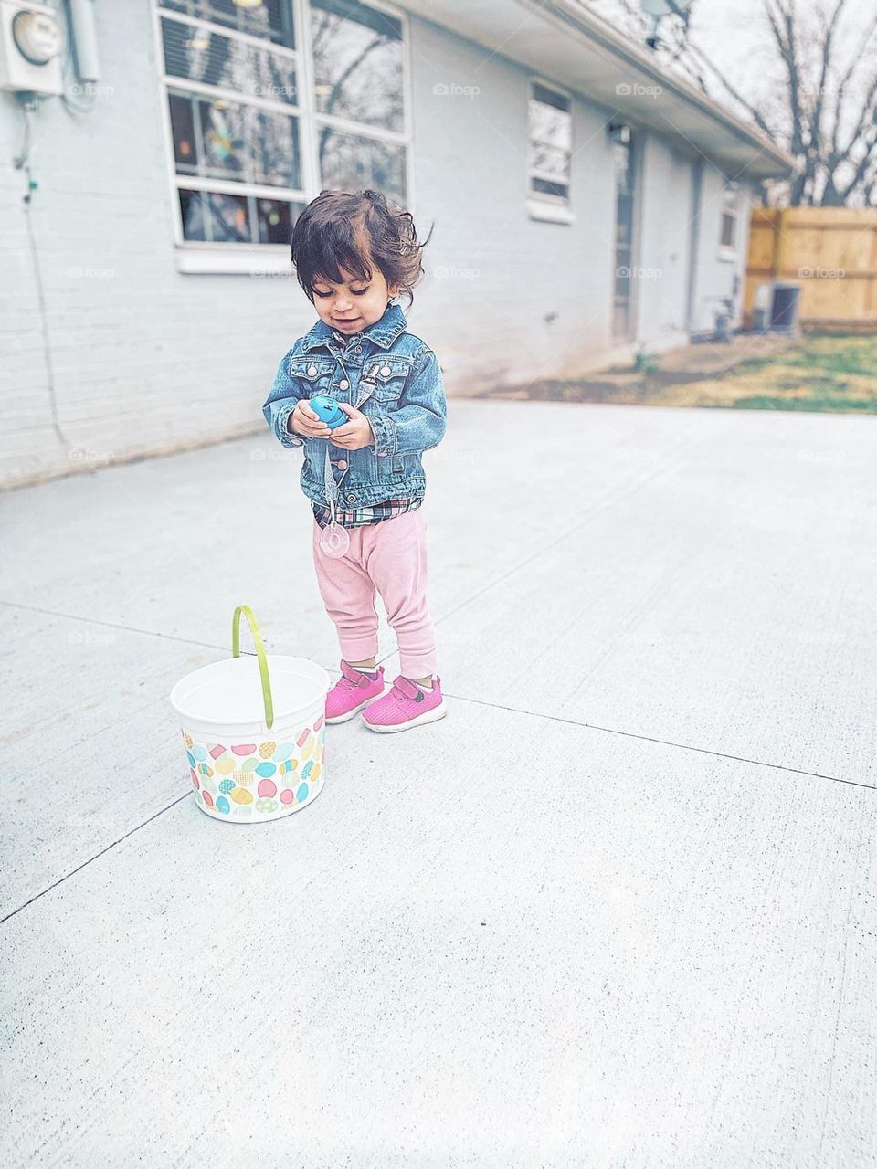 Toddler girl on Easter Egg Hunt, toddler girl picks up eggs, toddler girl proud of herself for picking up Easter Eggs, children on Easter Egg Hunts, Easter traditions, fun with family 