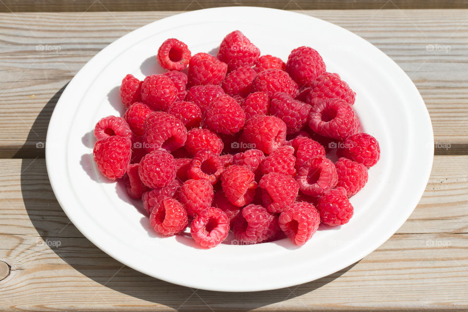 Raspberries on a white plate in sunny weather - solmogna hallon på vit tallrik 