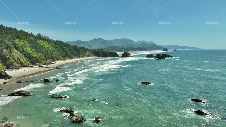 Flying above the Pacific right off the coast of Cannon Beach, the waves roll in with such strength and beauty while the beautiful Cascade Mountain Range Rises above with the smell of evergreen surrounding you