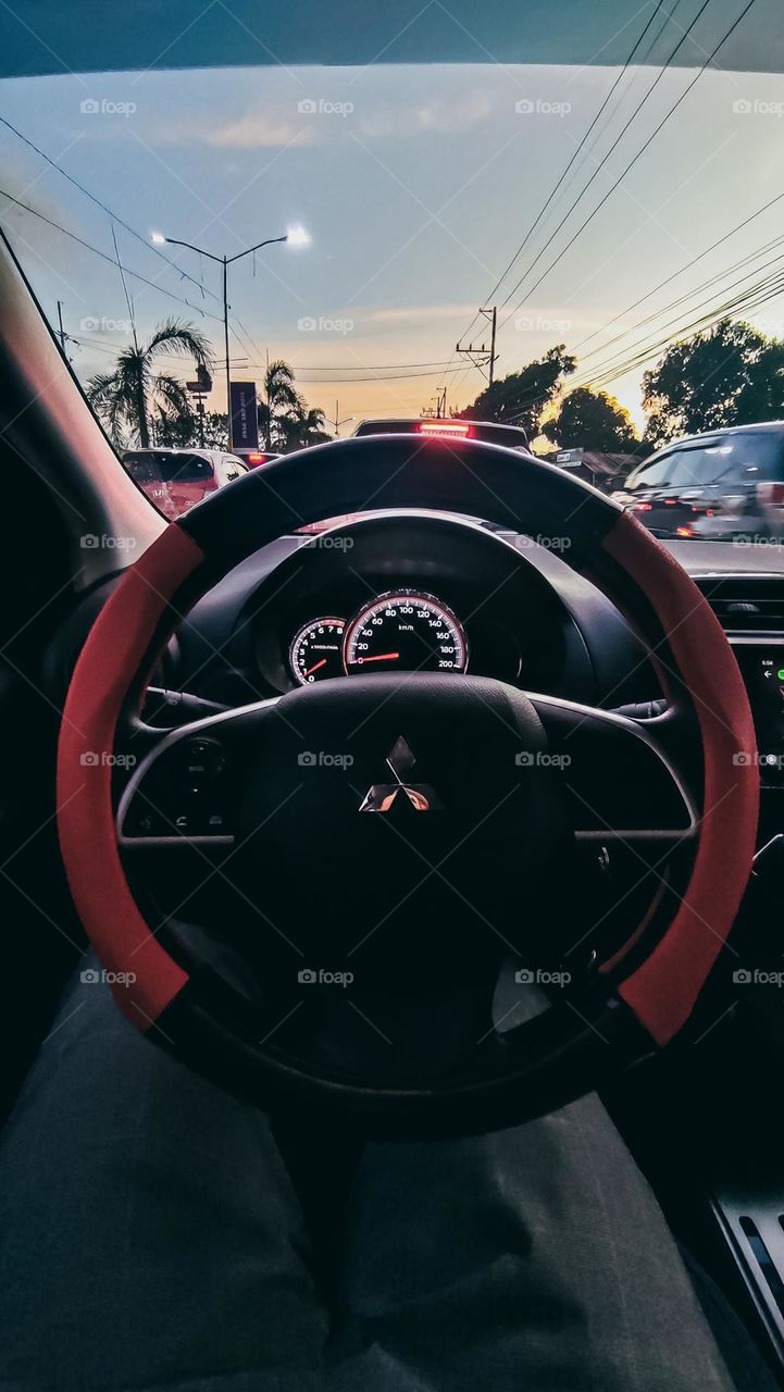 Commuting in a private car Mitsubishi Mirage Car with Red Steering wheel protector while in a traffic during sunset golden hour.