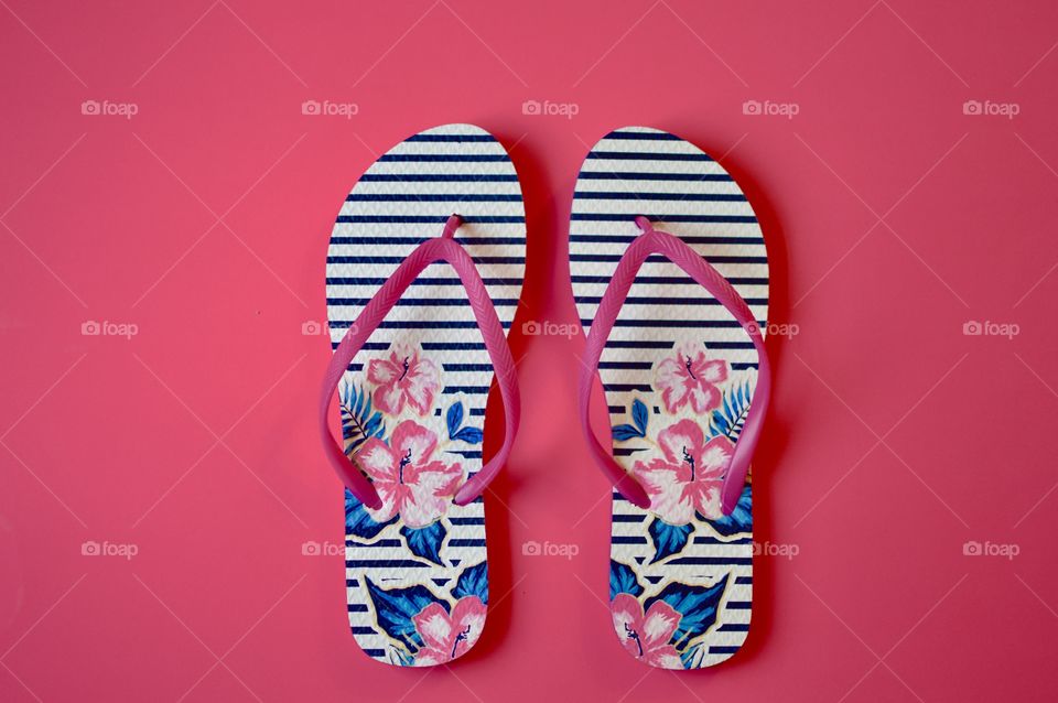 Contrasting flatlay with a pink background and pink blue black striped flip flops 