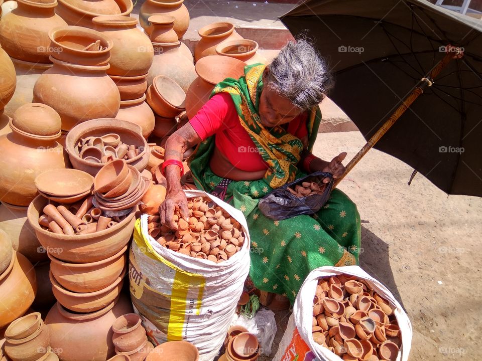 An Indian poor old women selling clay pots in summer on the street side.