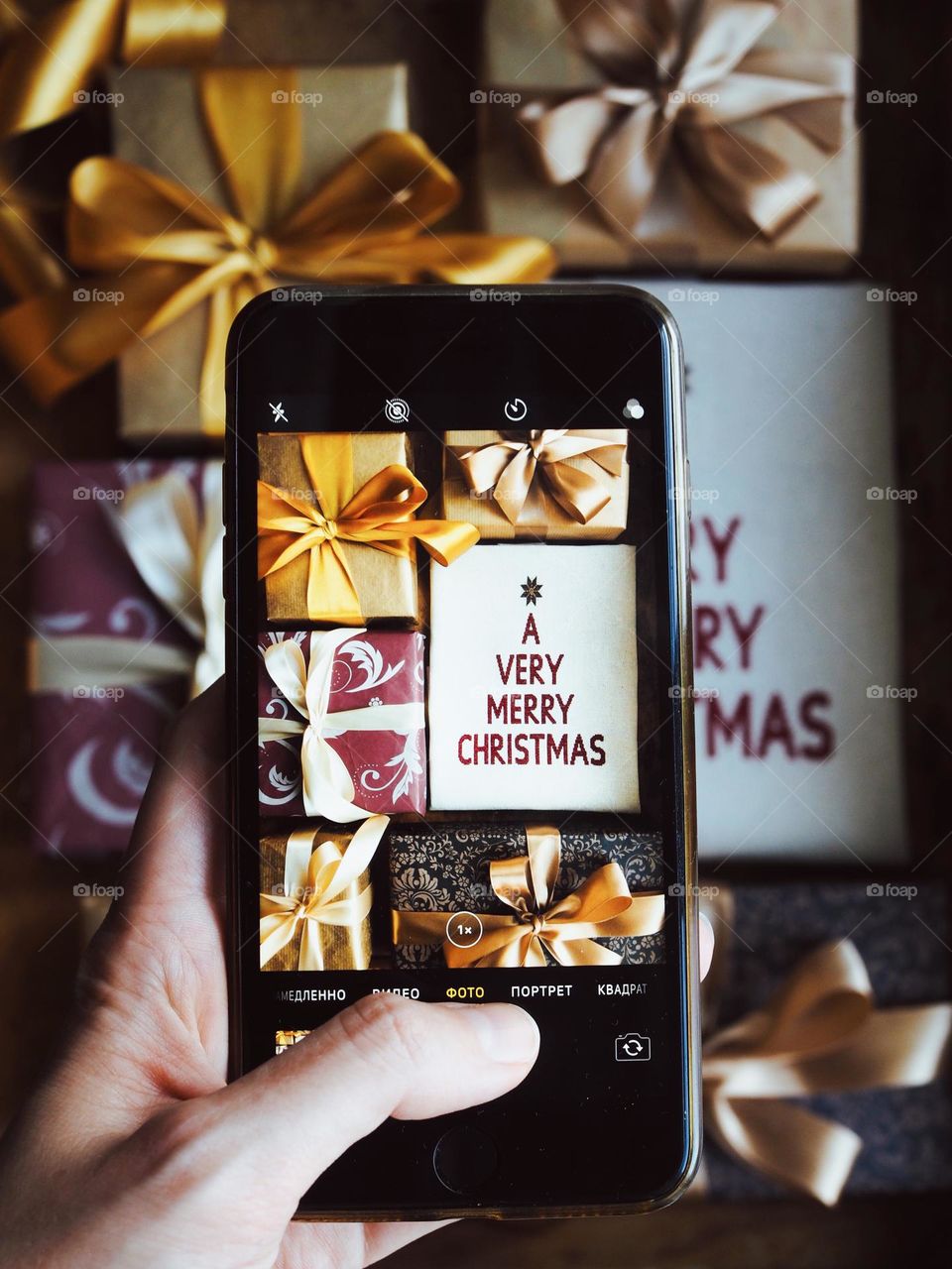 Female hand taking photo with smartphone of stylish wrapped Christmas gifts on wooden background. The girl taking a picture of a gifts on the phone. Christmas, New Year, social media, holiday concept, rectangle