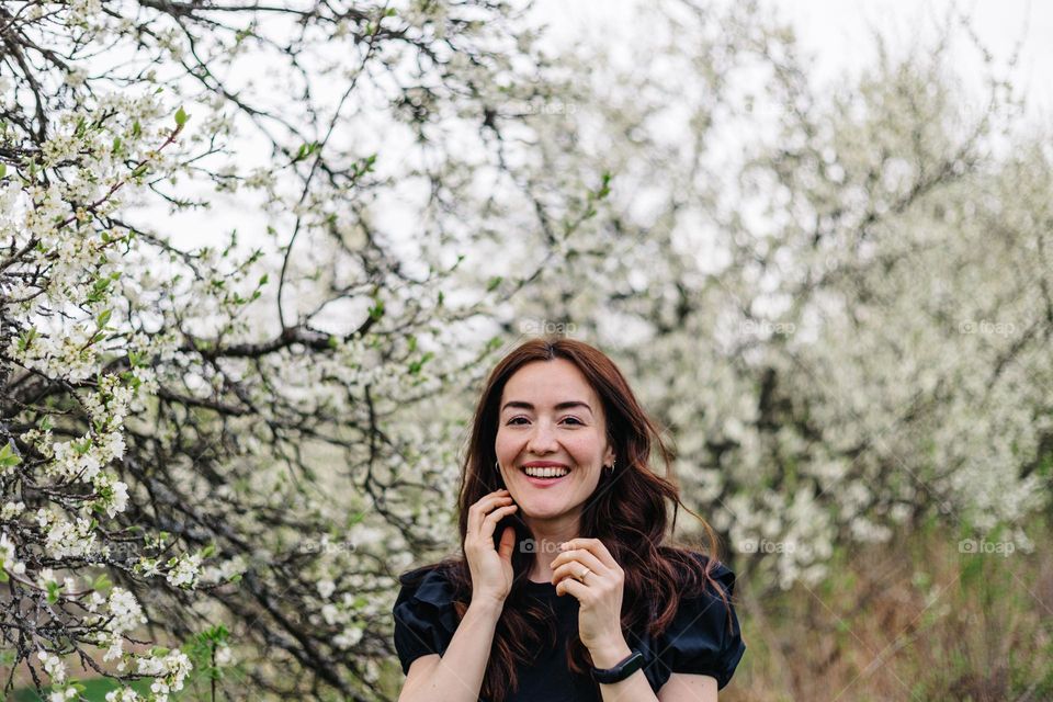 Woman smiling while on a walk in nature, surrounded by blossomed trees, during spring time.