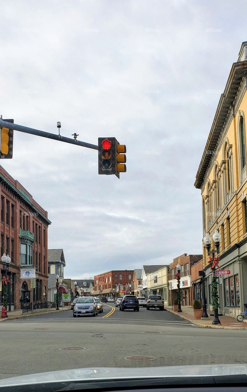 Town enter in the suburbs. Overhead traffic light is red, stop and wait for green. Pic of town center, no traffic, overcast day. Architecture of buildings from years in 1800's!