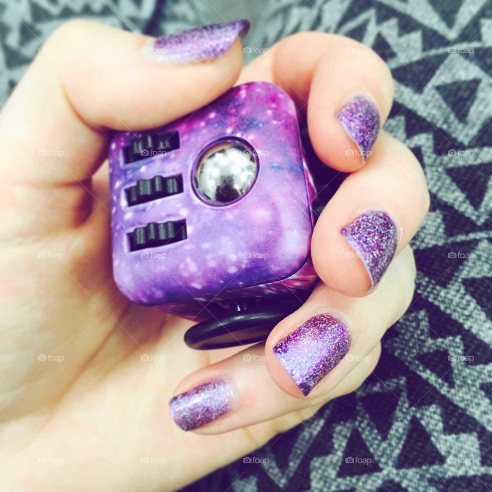 Purple galaxy fidgit cube hand activity held in a hand with purple sparky nail varnish polish