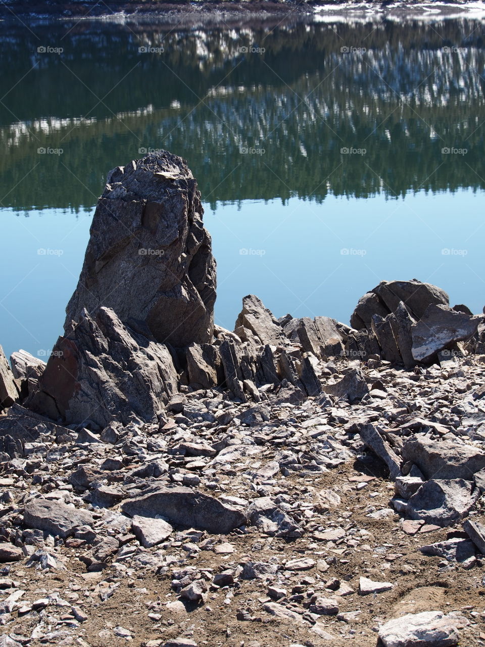 Jagged rocks and boulders along the shoreline of Ochoco Lake in Central Oregon on a sunny spring day.