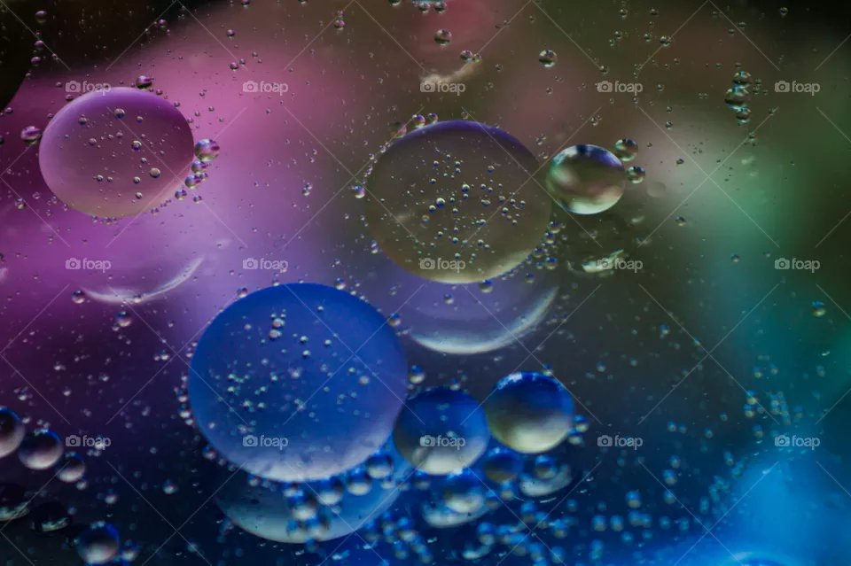Bubbles of vegetable oil in clear water on a glass and transparent lid from a frying pan on colored paper.