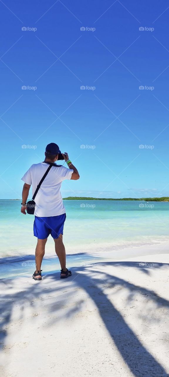 man taking photos of a totally paradisiacal beach landscape with white sands and crystal clear waters totally lonely