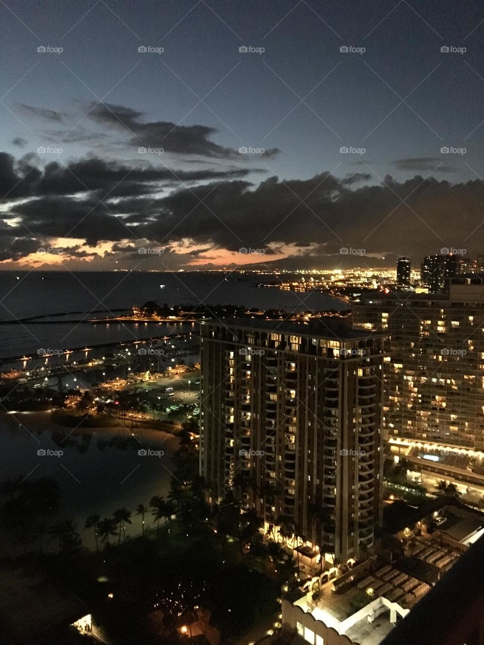 Honolulu Waikiki Hawaii just after sunset.  City lights, night life in tropical paradise.  Large billowing black clouds cover the last pieces of the sun over the ocean