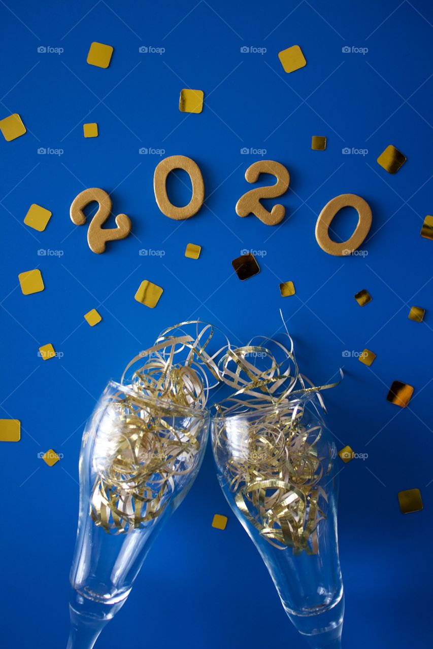 Conceptual flat lay of a champagne toast with glittering gold confetti and the numbers ‘2020’ in gold on a classic blue background - portrait format 